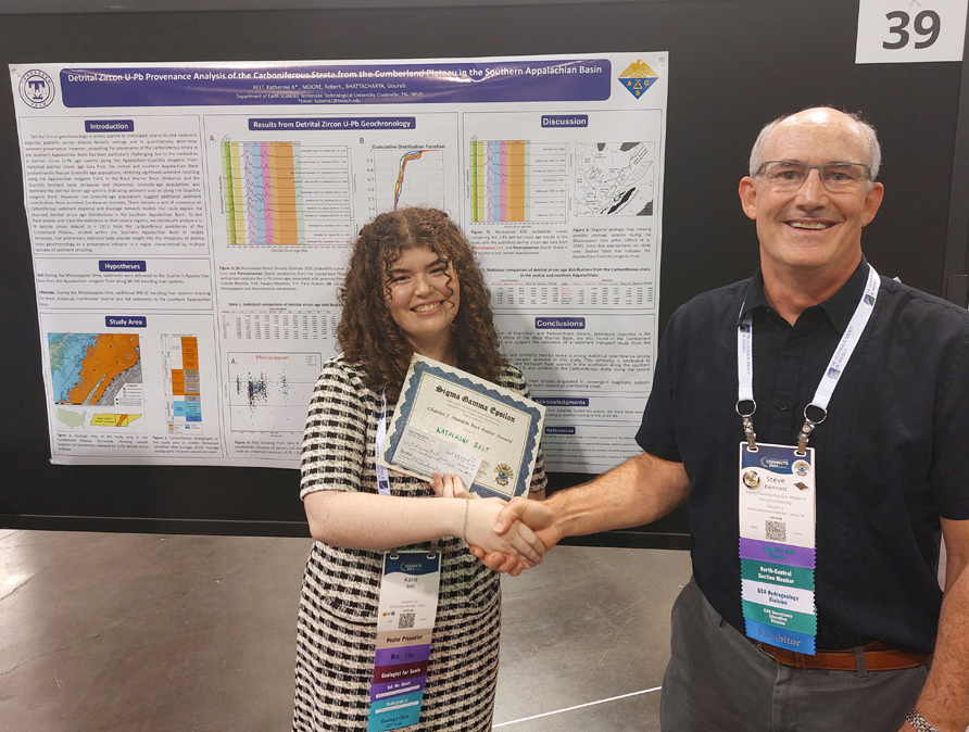 National President shakes hands with presenter.  They are standing in front of a research poster